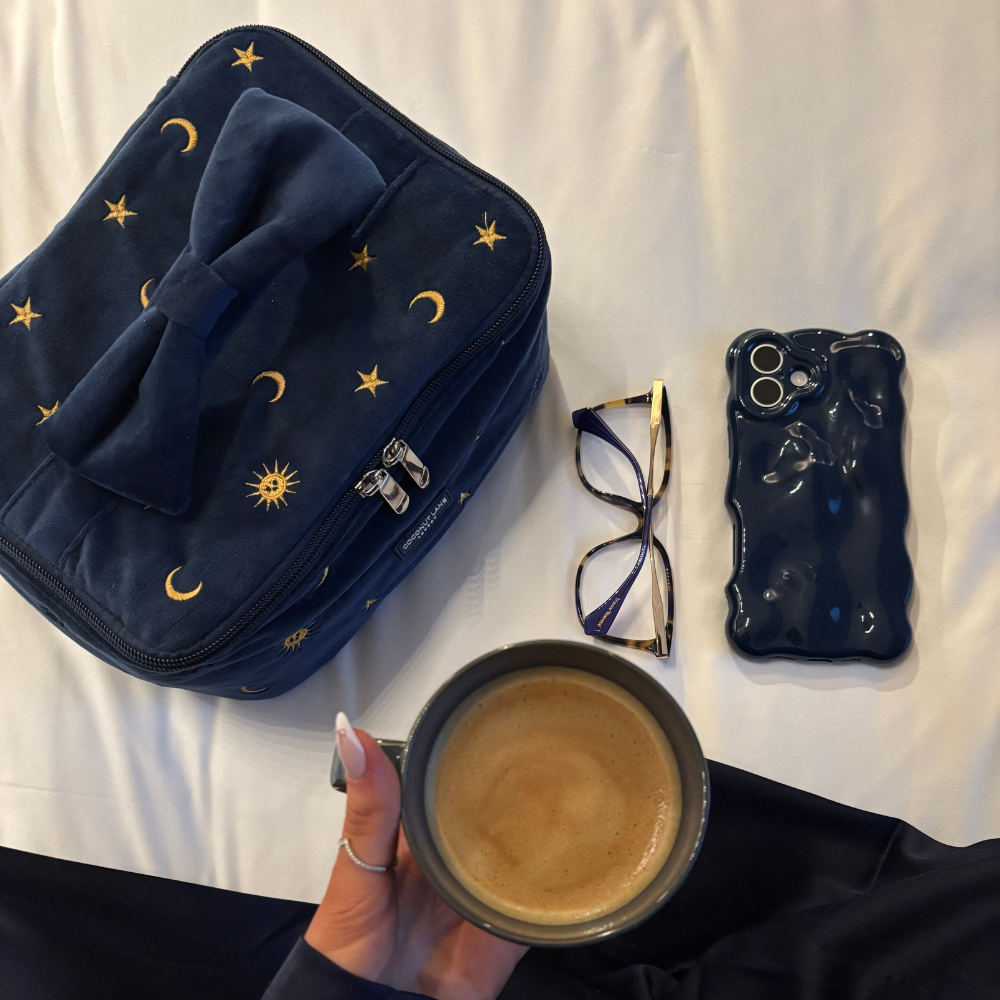 Navy 3D bubble phone case, starry navy bag, and glasses on a bed; hand holding coffee nearby.