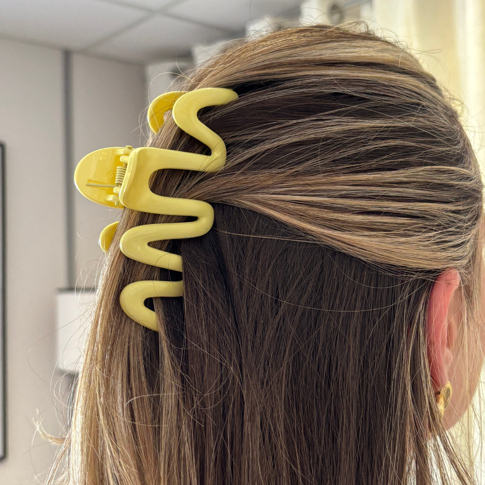 Blonde-haired person from behind wearing a yellow Coconut Lane squiggle claw clip indoors.