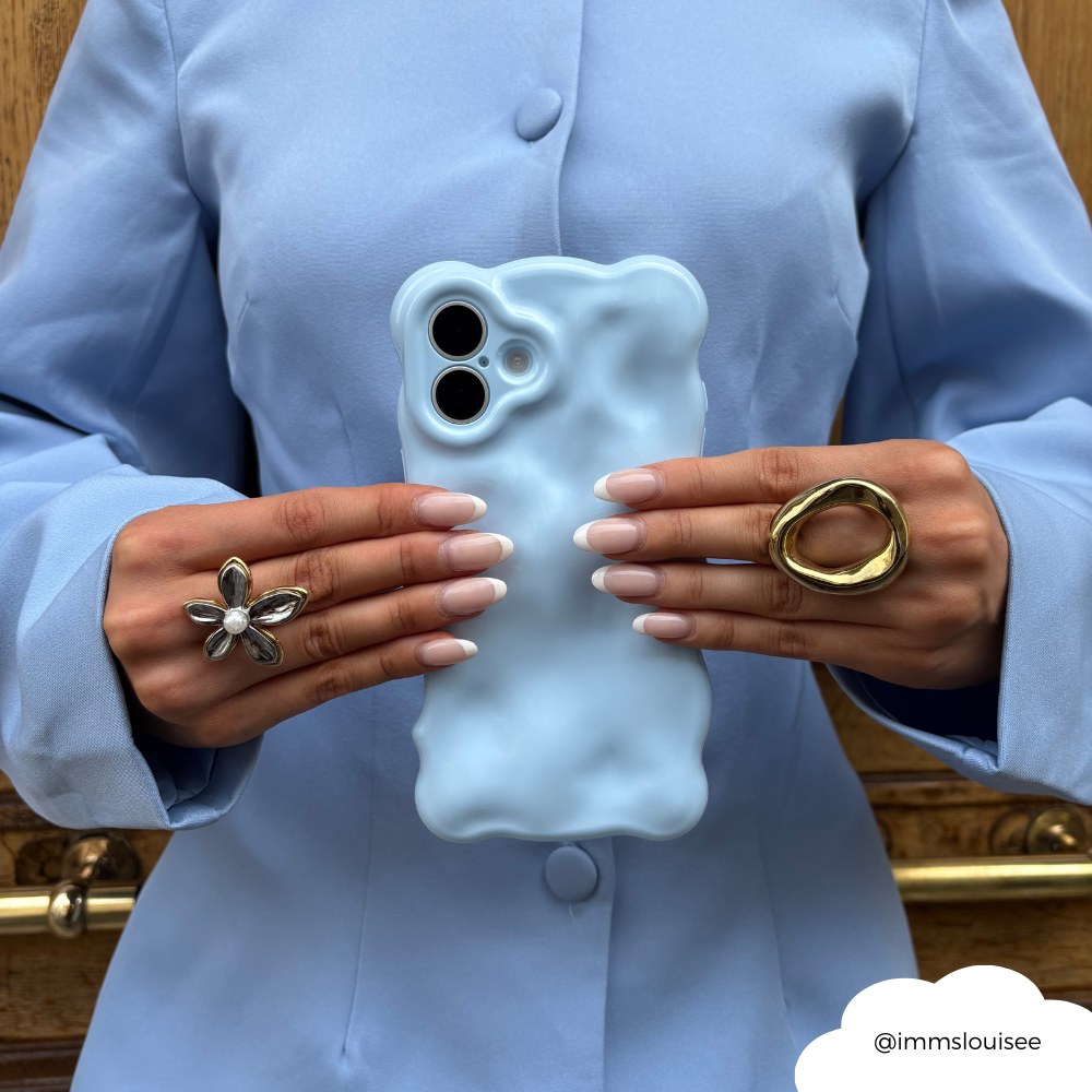 Woman in a light blue blazer holds a baby blue 3D bubble phone case, with bold silver and gold rings on her fingers.