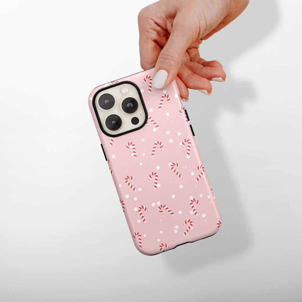 A hand with manicured nails holds a smartphone with a pink case decorated with small candy canes and white dots.