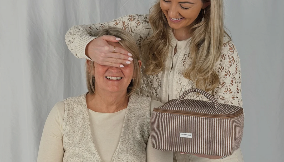 A pink and red striped fabric makeup bag with a handle and double zipper, labeled "Coconut Lane," sits on a neutral background.