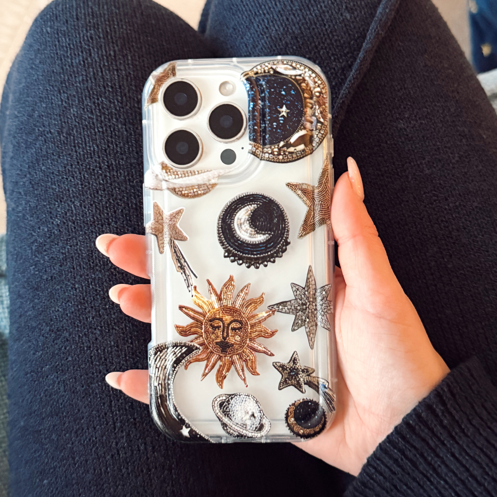 Clear phone case with sun, moon, star, and cloud designs held in a hand.