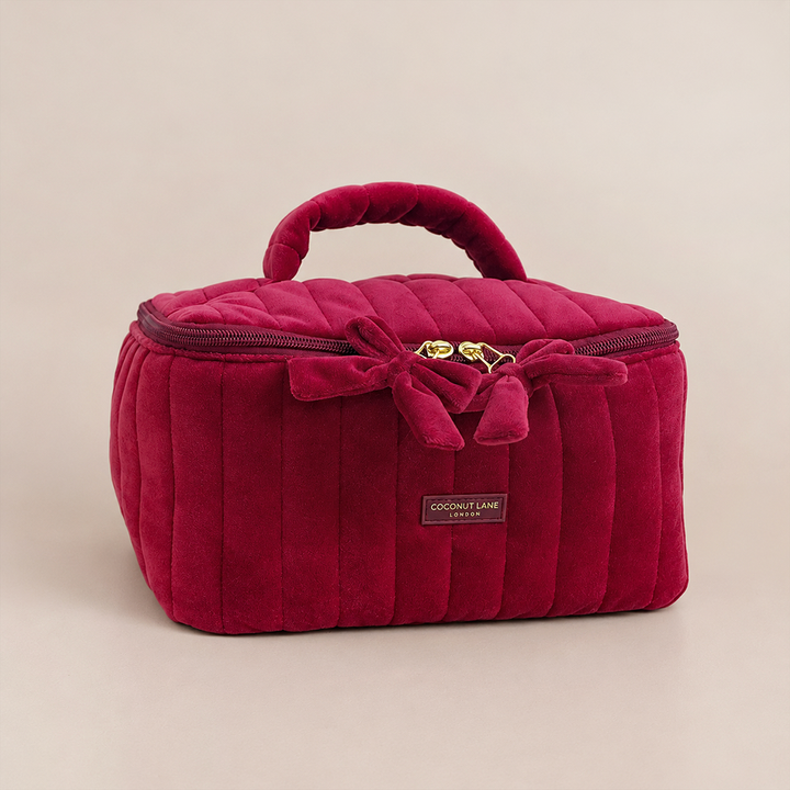 Burgundy velvet cosmetic bag with a quilted design, top handle, bow detail, and gold-tone hardware.
