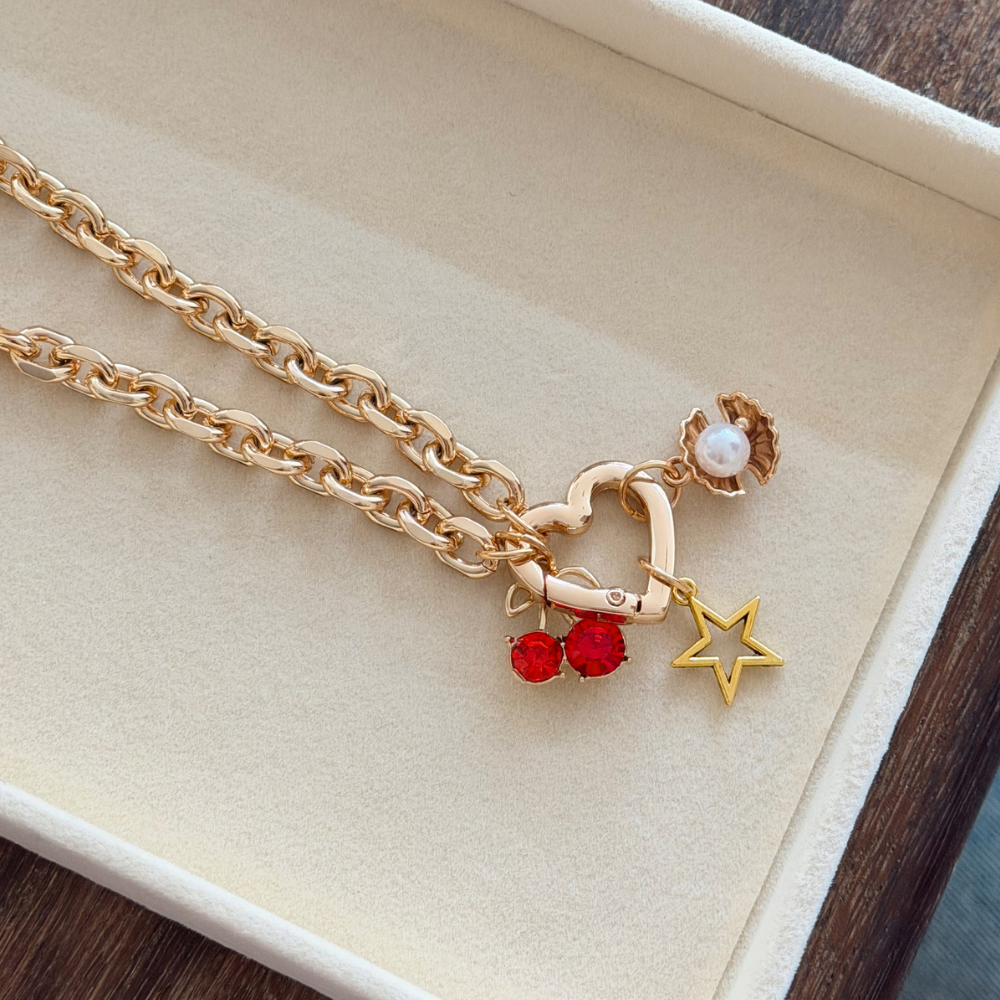 Gold Phone Strap with heart, cherry, and star charms on a beige background