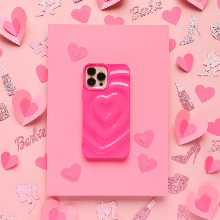 The Melting Heart Phone Case - Bright Pink by Coconut Lane is showcased on a matching background, adorned with heart-shaped decorations, glittery "Barbie" text, and sparkling images of high heels, lipstick, and a horse. The scene is predominantly pink and captures a playful, girly vibe.