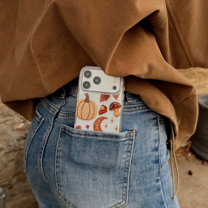 A person wearing a brown suede jacket and light blue jeans, shown from the back. With the Fall for It Clear Case decorated with autumn-themed beaded effect designs including pumpkins, acorns, mushrooms, leaves, and a pumpkin spice coffee cup, tucked into the back pocket