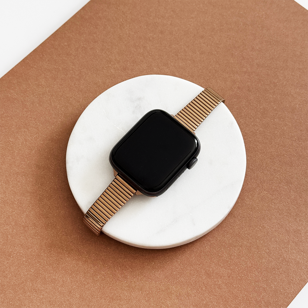 Rose gold Coconut Lane slim Apple Watch strap with fine lines displayed on a white marble surface.