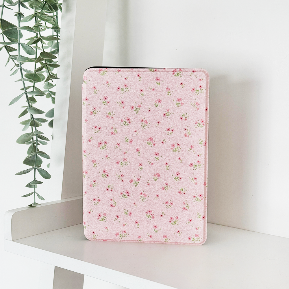 Pink Kindle case with ditsy floral pattern next to green eucalyptus leaves.