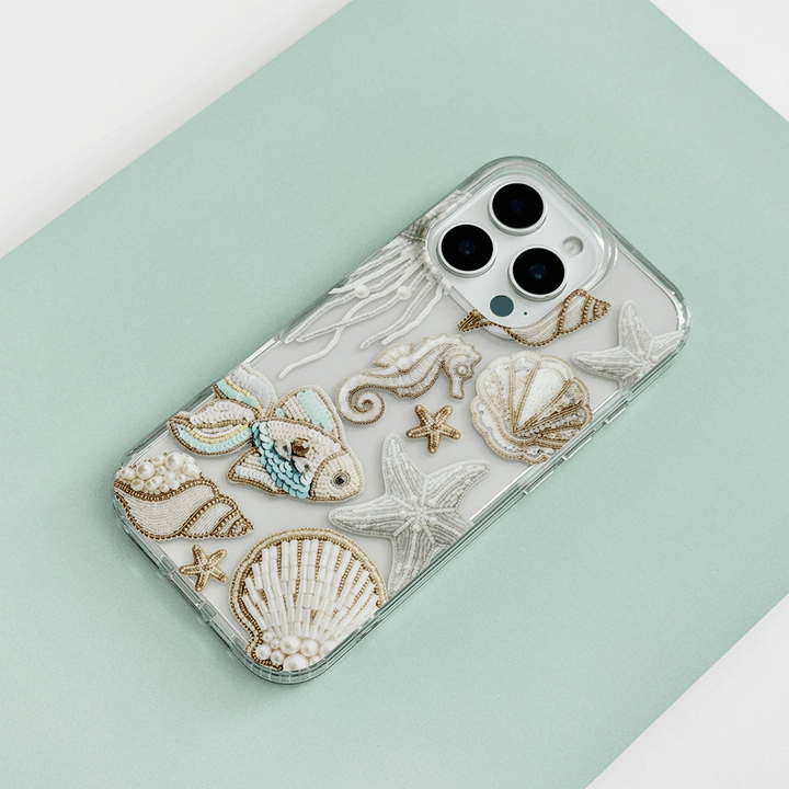 Clear phone case in mint green with embroidered seashell, fish, and starfish motifs.