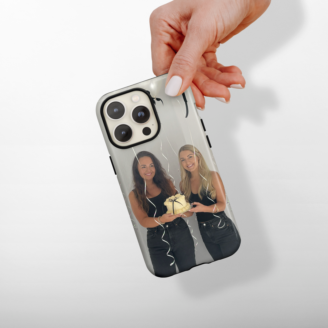 Phone case with two women holding a cake, held by a hand on a white background