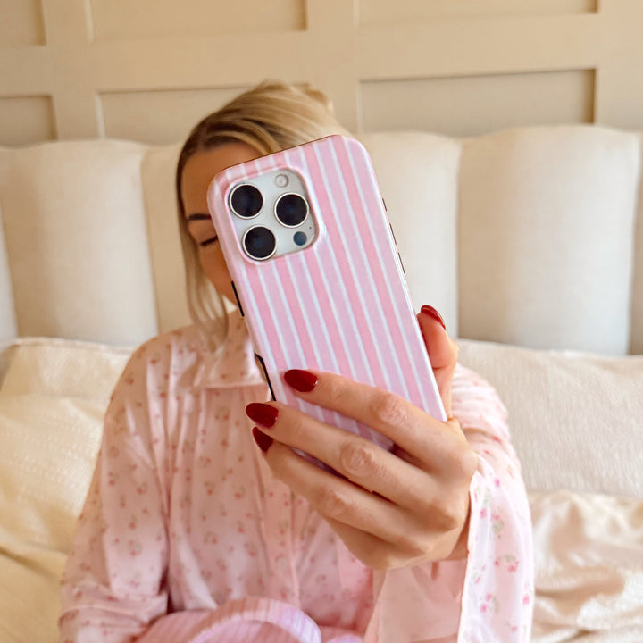 Girl holding a powder stripes phone with a pink case on a bed and pink pjs.