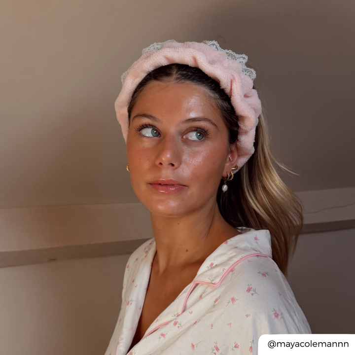 A woman wearing a light pink plush headband with a lace trim and a matching white floral pajama top with pink trim, looking to the side.
