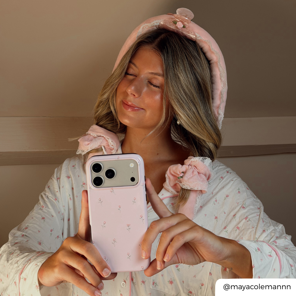 A woman takes a mirror selfie wearing a pink floral pyjamas and a pink pointelle heatless curls set. She holds a light pink phone case with a small floral pattern.