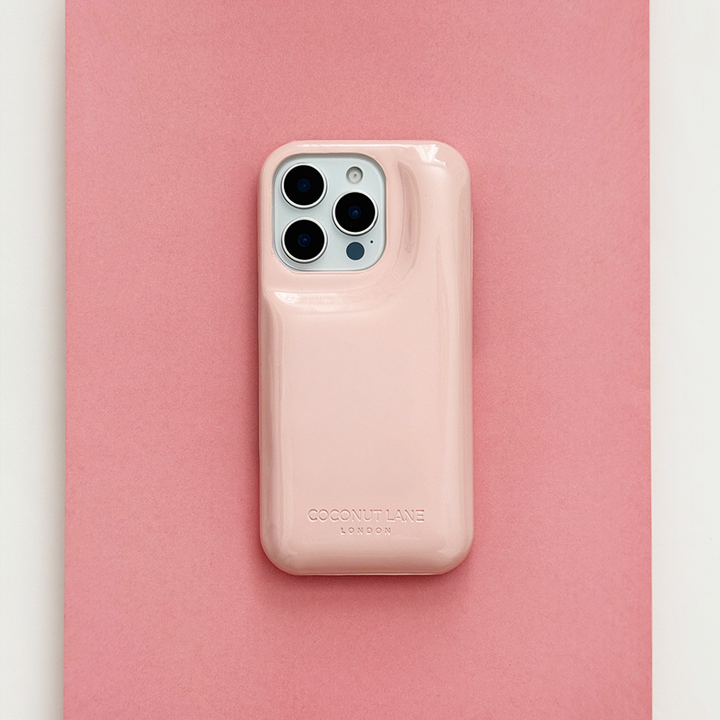 Glossy pastel pink Coconut Lane puffer phone case with embossed logo, displayed diagonally on a matching pink background.