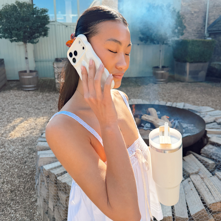 Girl sipping out of her milky coconut stainless steel tumbler in front of a fire pit in spring time