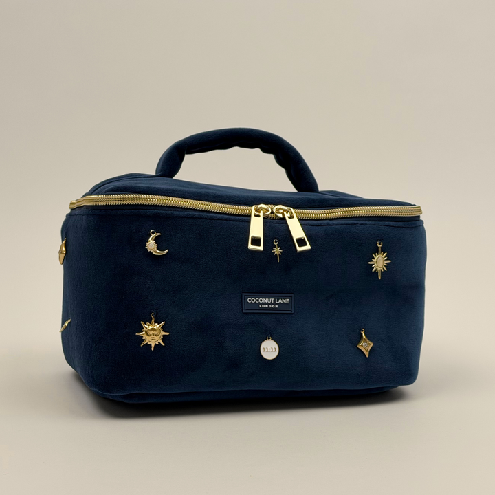 Stardust After Dark Vanity Case. A dark blue navy velvet vanity case with gold zip, and sewn-on gold celestial-themed charms. Including a moon, sun, star, diamond shape and 11:11 charm. 