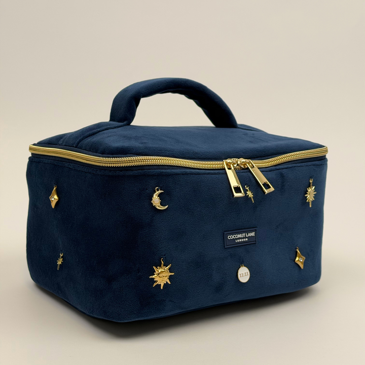 Stardust After Dark Vanity Case. A dark blue navy velvet vanity case with gold zip, and sewn-on gold celestial-themed charms. Including a moon, sun, star, diamond shape and 11:11 charm. 