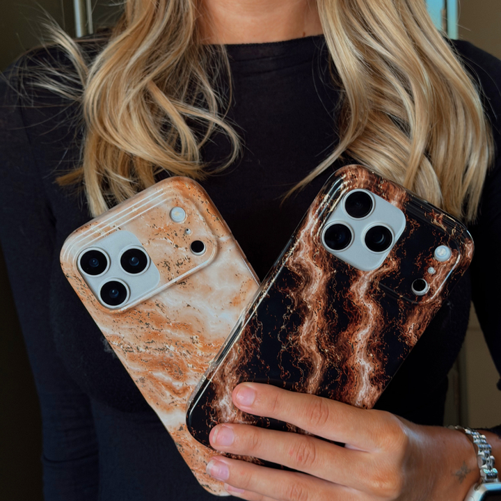 A woman holds two iPhone cases with a marble pattern. One case has a light beige and white marble design with subtle gold glitter flecks, and the other has a dark brown marble design with gold flecks.