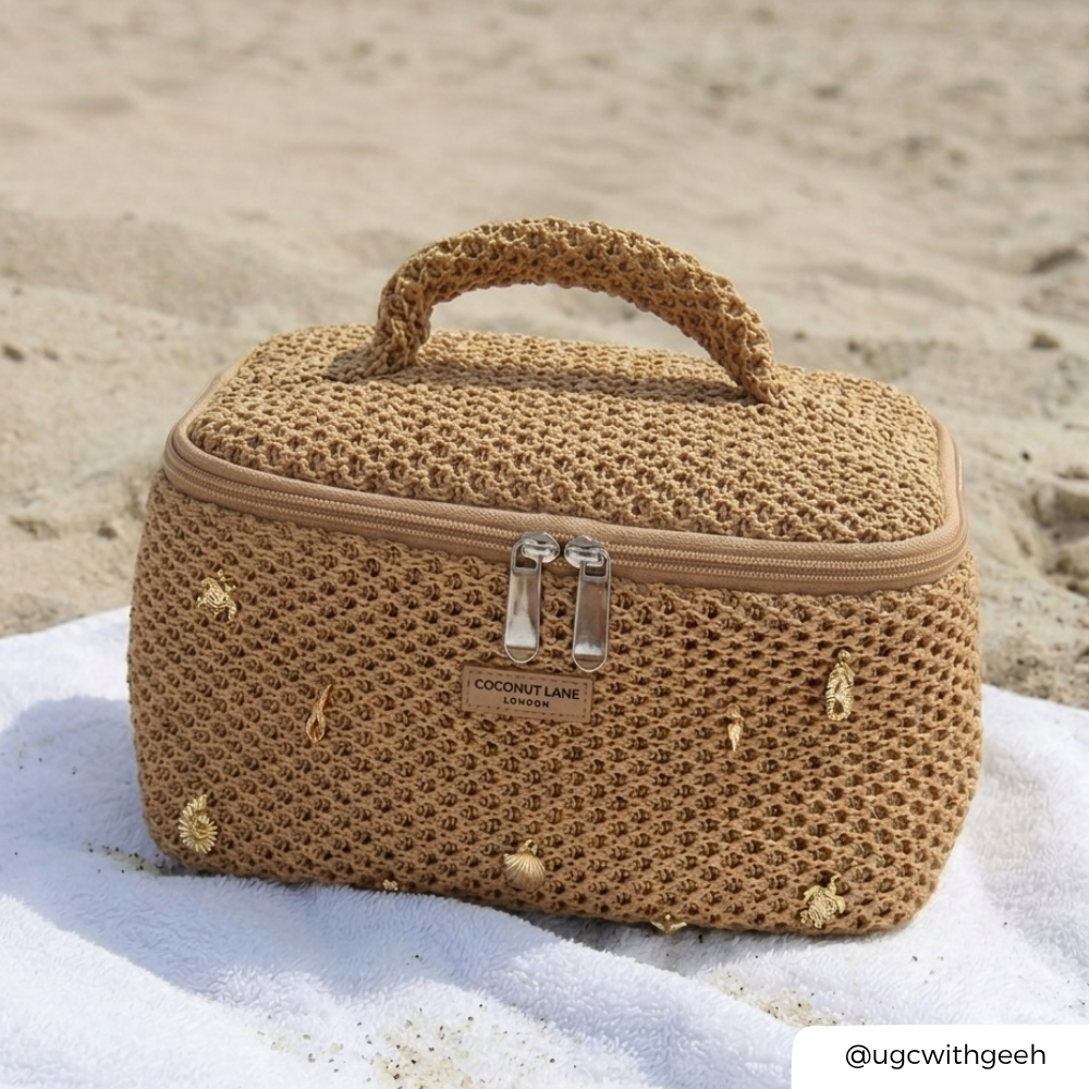 Woven beige makeup bag with a visible brand logo on a sandy background with gold shells