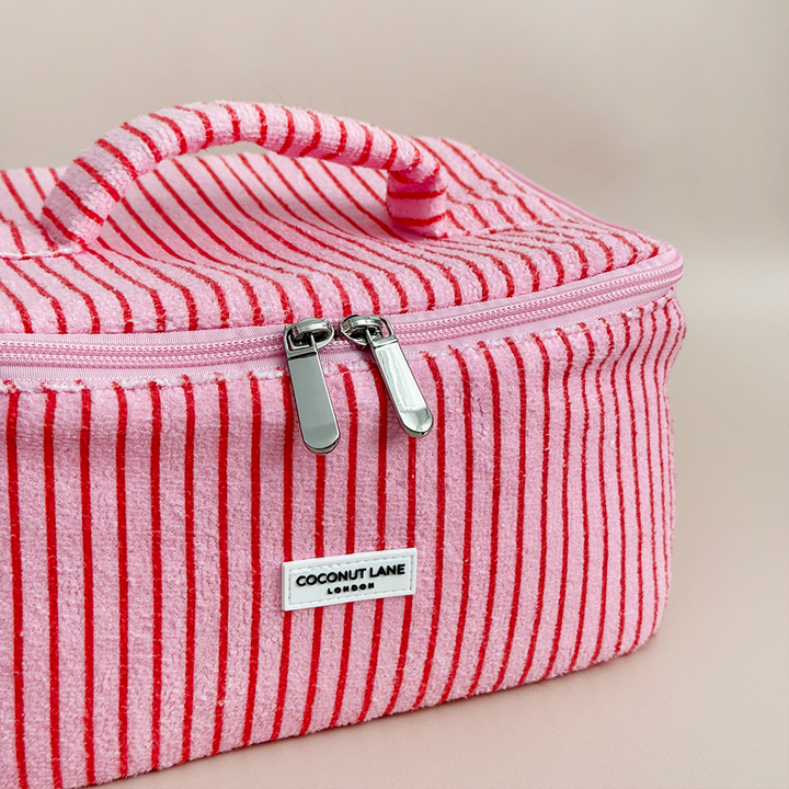 Pink and red striped toiletry bag with Coconut Lane brand label on a beige background