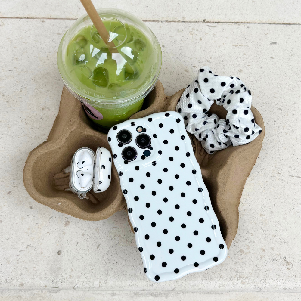 White polka dot wavy phone case next to a green drink, scrunchie, and earbuds on a tray.