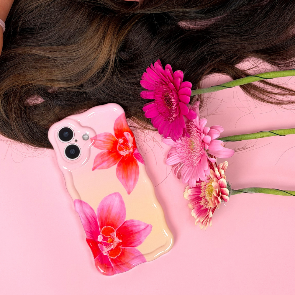 Phone case with floral design held by a person with flowers on a pink background