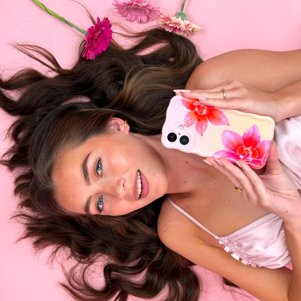 Woman holding a phone with a floral case on a pink background