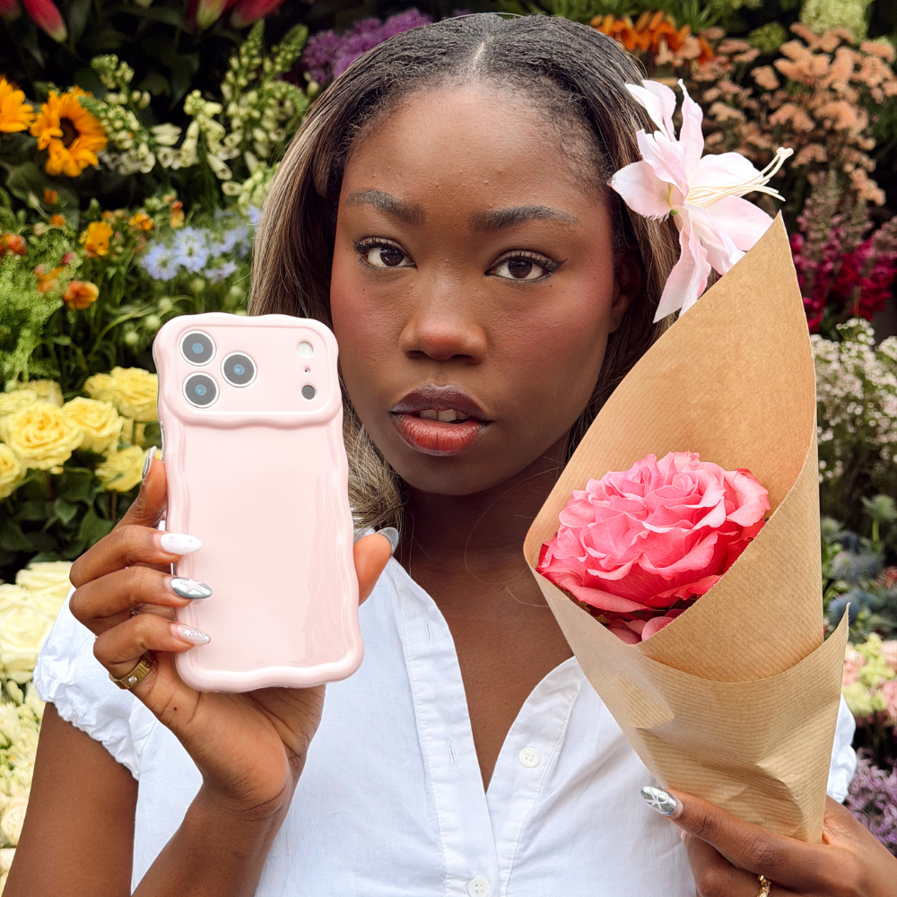 Girl showing off wavy pink phone case next to her pink flower and a flower stand