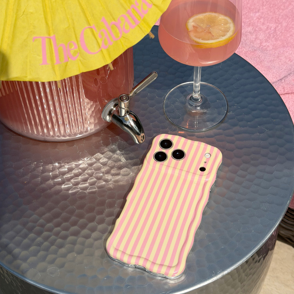 Wavy Phone case with pink and yellow striped pattern on a table with a cocktail and umbrella.