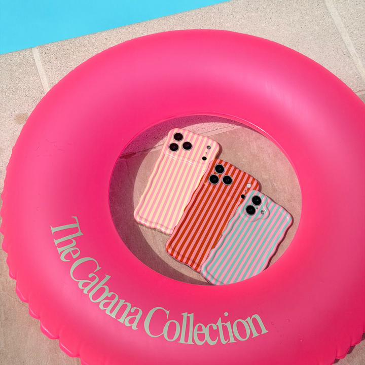 Three striped phone cases on a pink inflatable ring with 'The Cabana Collection' text.