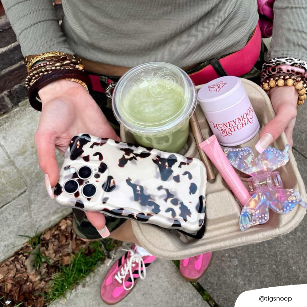Girl holding coffee cup holder with Wavy Ivory Tort phone case, a matcha, lipgloss and hair clip.