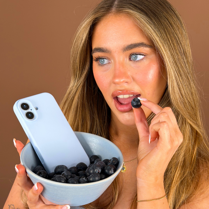 Girl biting blueberry with the butter soft silicone phone case in a blue bowl
