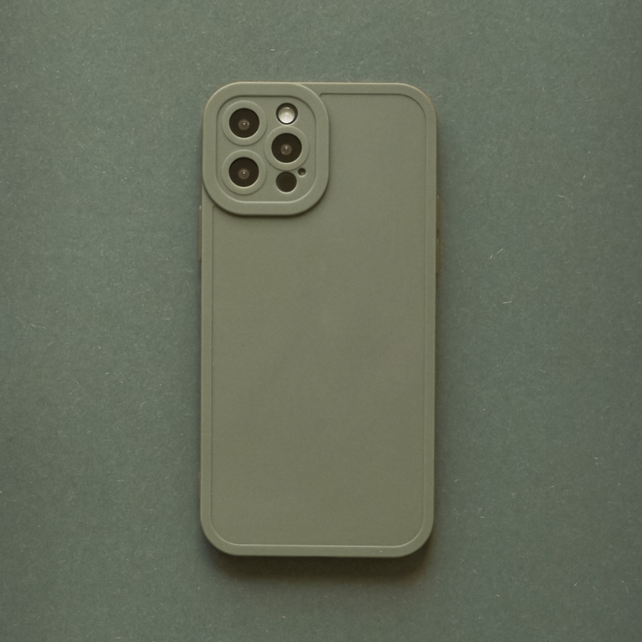 A phone case named the NAKD Phone Case - Khaki by Coconut Lane is shown facing down, highlighting its four-camera setup on the top left corner. The khaki-colored, matte finish case is placed on a textured surface that matches the color of the device, epitomizing minimalism while ensuring full camera protection.