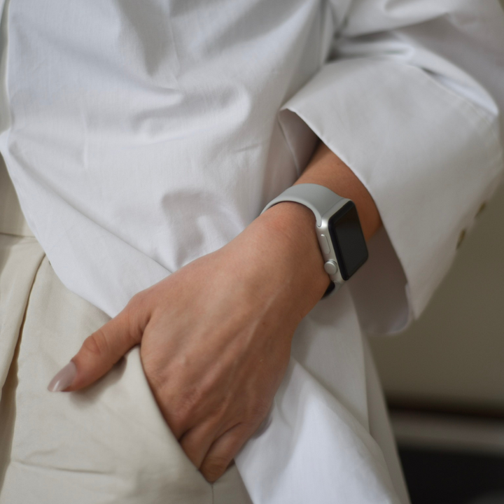 Close-up of a person wearing a white shirt and light-colored pants, with their left hand in their pocket. They are sporting the NAKD Apple Watch Strap - Ice Grey by Coconut Lane on their wrist. The scene exudes a casual yet professional vibe.