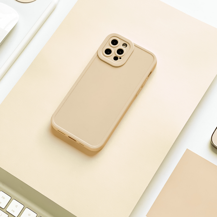 A beige smartphone with a Coconut Lane NAKD Phone Case - Nude lies flat on a cream-colored surface. Surrounding it are parts of a keyboard, a mouse, and various other office supplies, all in a similar neutral color scheme. The soft flexible TPU material ensures full camera protection, creating a cohesive and minimalist aesthetic.