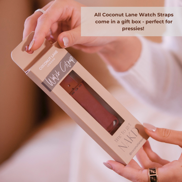 A person is holding a Coconut Lane gift box, which contains an Almond White NAKD Apple Watch Strap. The beige box reads "time to get NAKD" and has a window displaying the strap inside. A caption in the image says, "All Coconut Lane Watch Straps come in a gift box - perfect for pressies!
