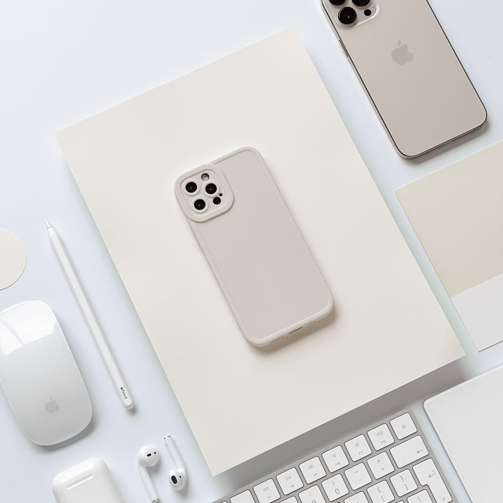 A neatly arranged flat lay featuring gray and white tech accessories, including an iPhone with the NAKD Phone Case - Creamy White from Coconut Lane, a MacBook, AirPods, a Magic Mouse, an Apple Pencil, a keyboard, and a blank notebook—all set against a minimalist white background.